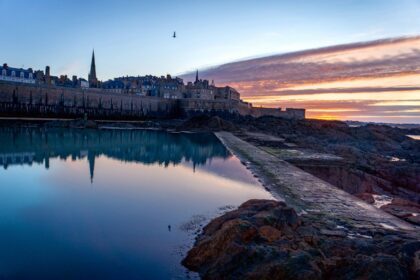 Sunrise over coastal medieval cityscape with reflections.